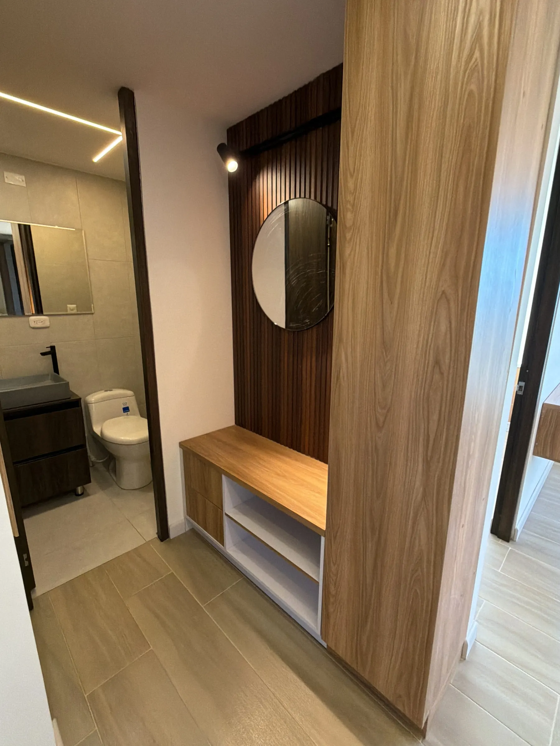 Vista del baño con revestimiento de listones de madera y mueble suspendido.