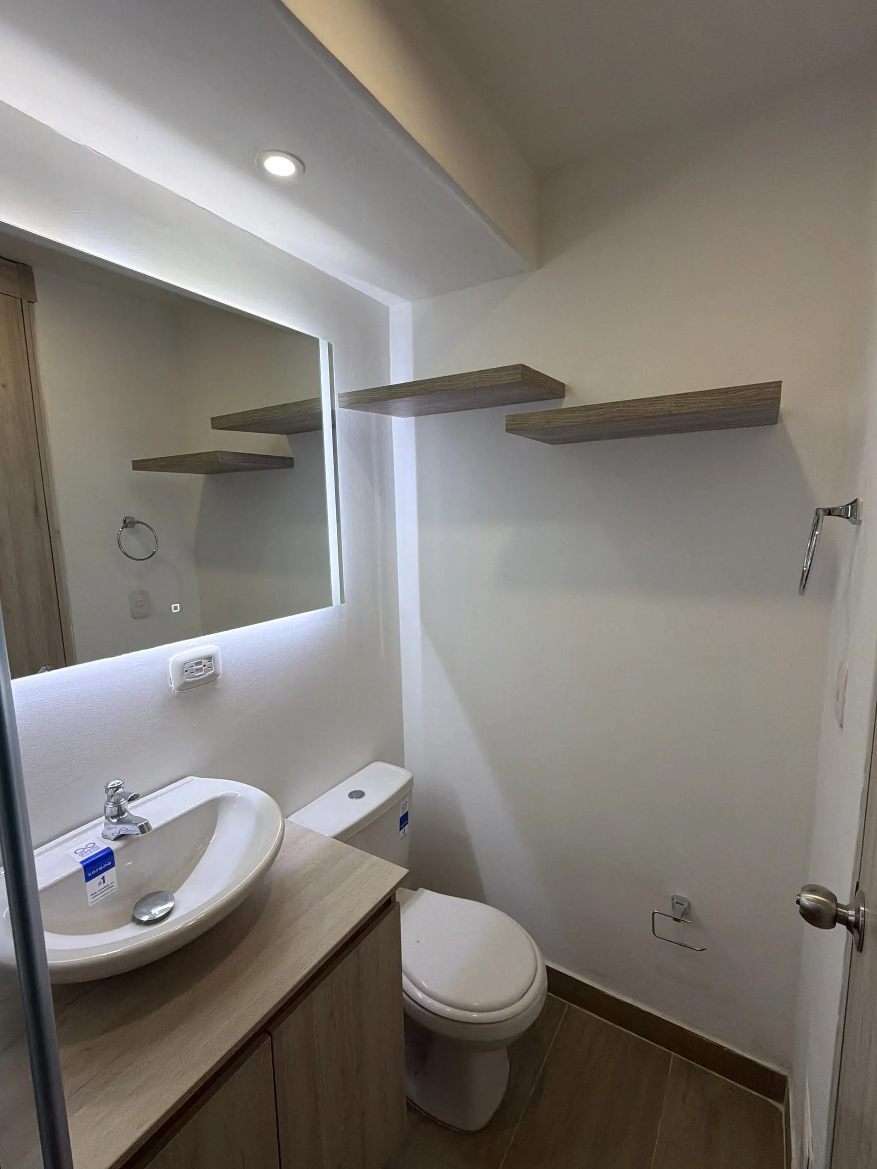 Baño con espejo retroiluminado, repisas voladas y mueble suspendido.