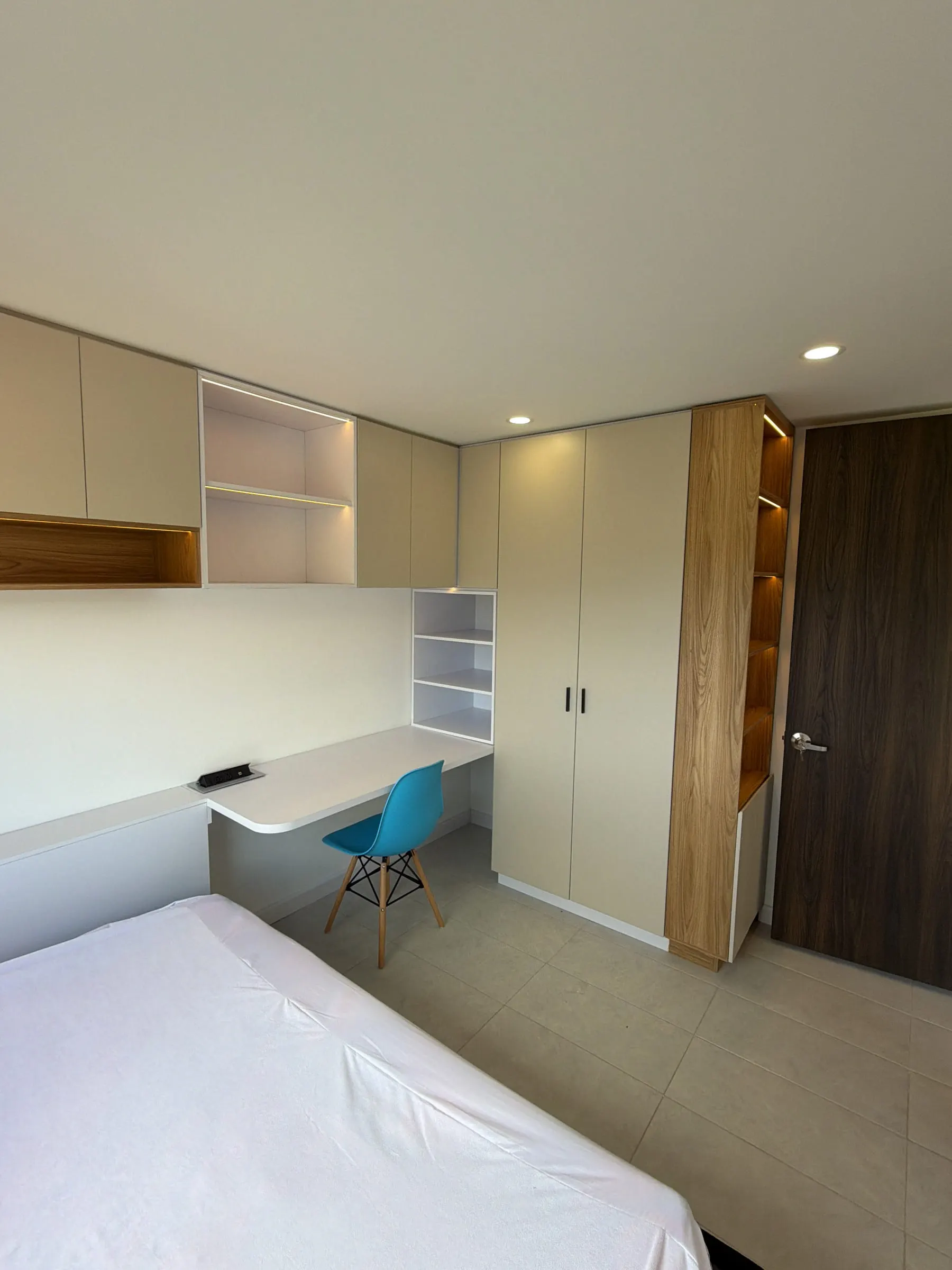 Habitación desde el otro extremo: escritorio bajo alacenas iluminadas, clóset y repisas en madera.